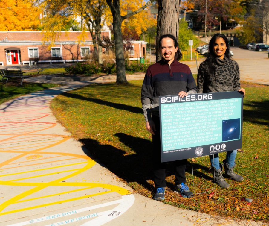 Chelsie and Daniel at Valley Court Park. They are holding the sign with the description of their artwork and they are standing by the Rainbow DNA art