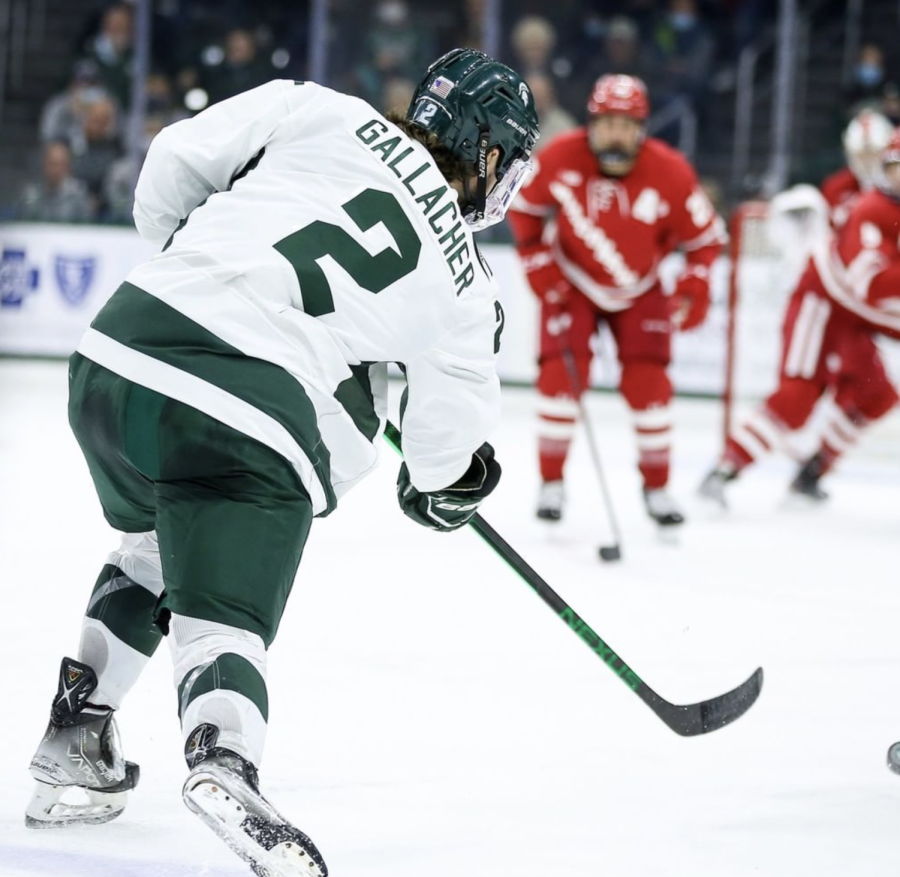 MSU+forward+Aiden+Gallacher+shoots+a+puck+towards+the+net+against+Wisconsin+in+2022%2F+Photo+Credit%3A+MSU+Athletic+Communications+