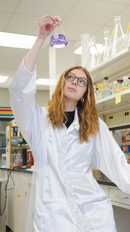 Maddy Eischer in lab holding a beaker that has purple liquid