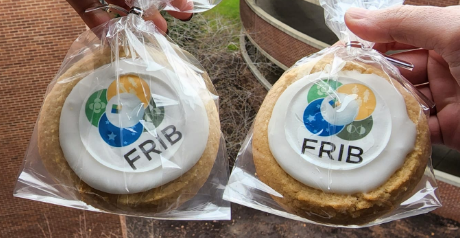 Sugar cookies with the FRIB logo printed on the cream on top of the cookie. The background of the photo is an overlook of the parking garage of the Wharton Center for Performing Arts.