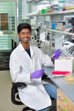 Hariharan Ramakrishnan sitting in a laboratory with a pipette in his hand with purple gloves on 