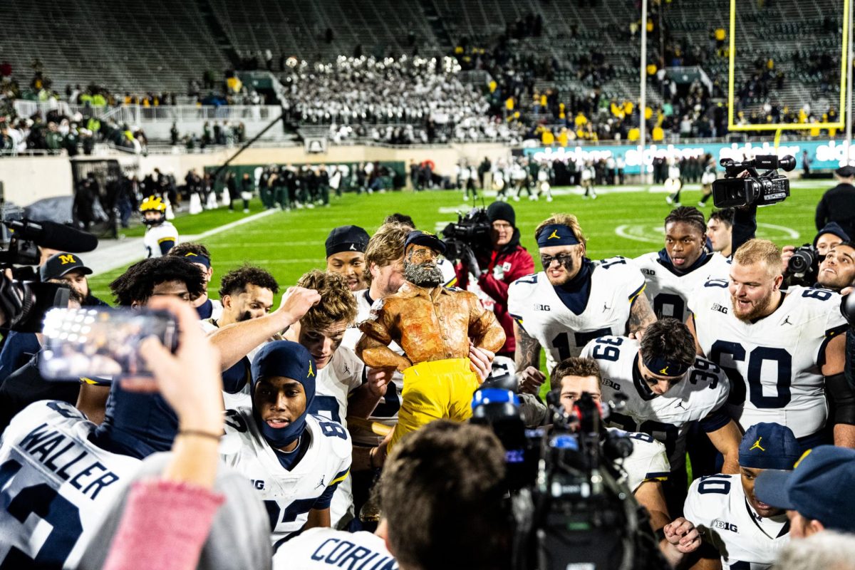 Michigan players hoist the Paul Bunyan Trophy after beating MSU 49-0 on Saturday, October 21, 2023 at Spartan Stadium.