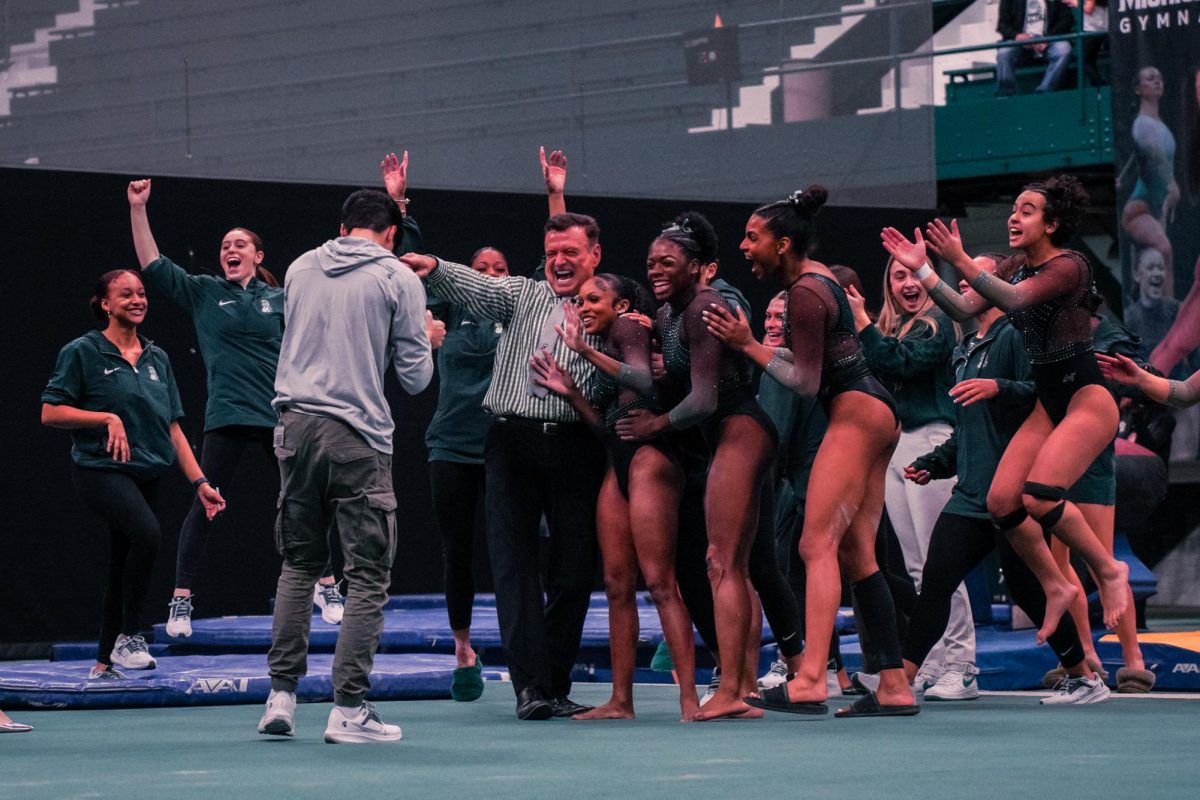 MSU+Head+Coach+Mike+Rowe+%28striped+shirt%29+celebrates+with+his+team+after+sophomore+Nikki+Smith+%28right+of+Rowe%29+scored+a+perfect+10+on+the+floor+for+the+Spartans+in+a+victory+over+Iowa+on+Sunday%2C+Jan.+28%2C+2024+at+Jenison+Field+House.
