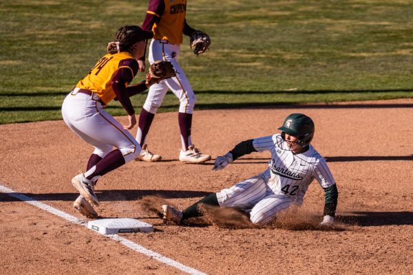 Hannah Hawley sliding to third base while Grace Koenig waits for the infield play to get Hawley out. (East Lansing, March 26, 2025). 