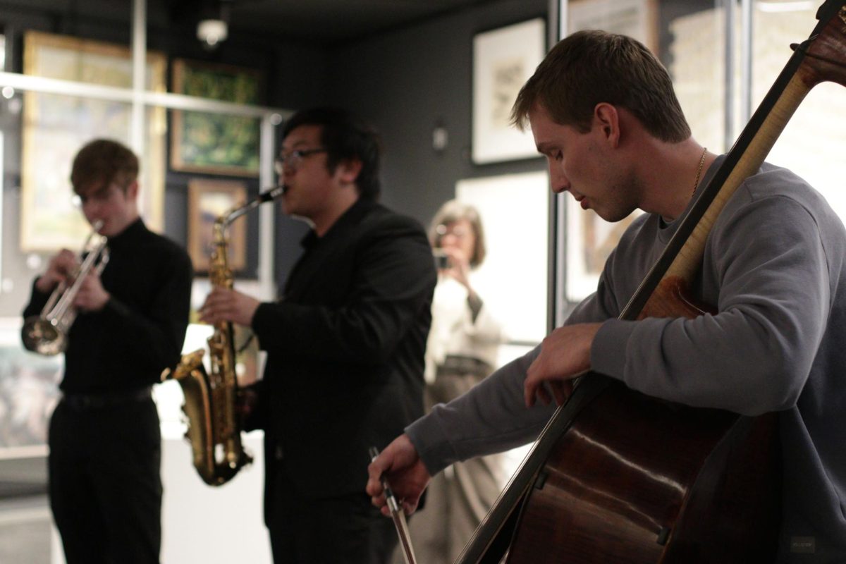 Three student performers are playing a cello, saxophone and trumpet respectively (right to left). 